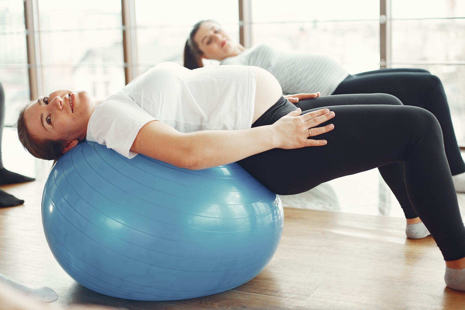 woman in white t shirt and black leggings stretching on blue exercise ball